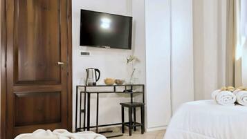 Une chambre d’hôtel avec une porte en bois, un téléviseur à écran plat fixé au mur, une petite table avec une bouilloire et des objets décoratifs, un lit avec des serviettes pliées et une grande armoire.