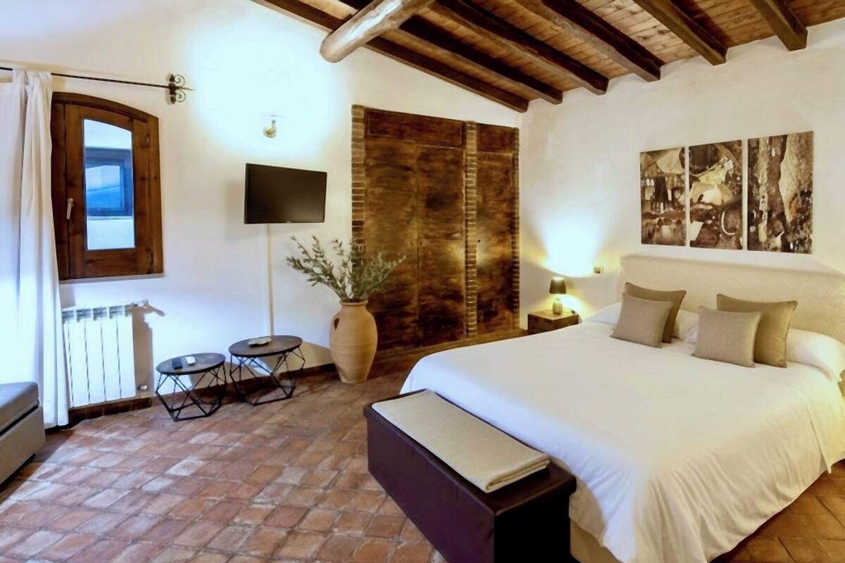 Une chambre à coucher avec un grand lit, une petite table, une plante en pot, un téléviseur et un panneau mural en bois.
