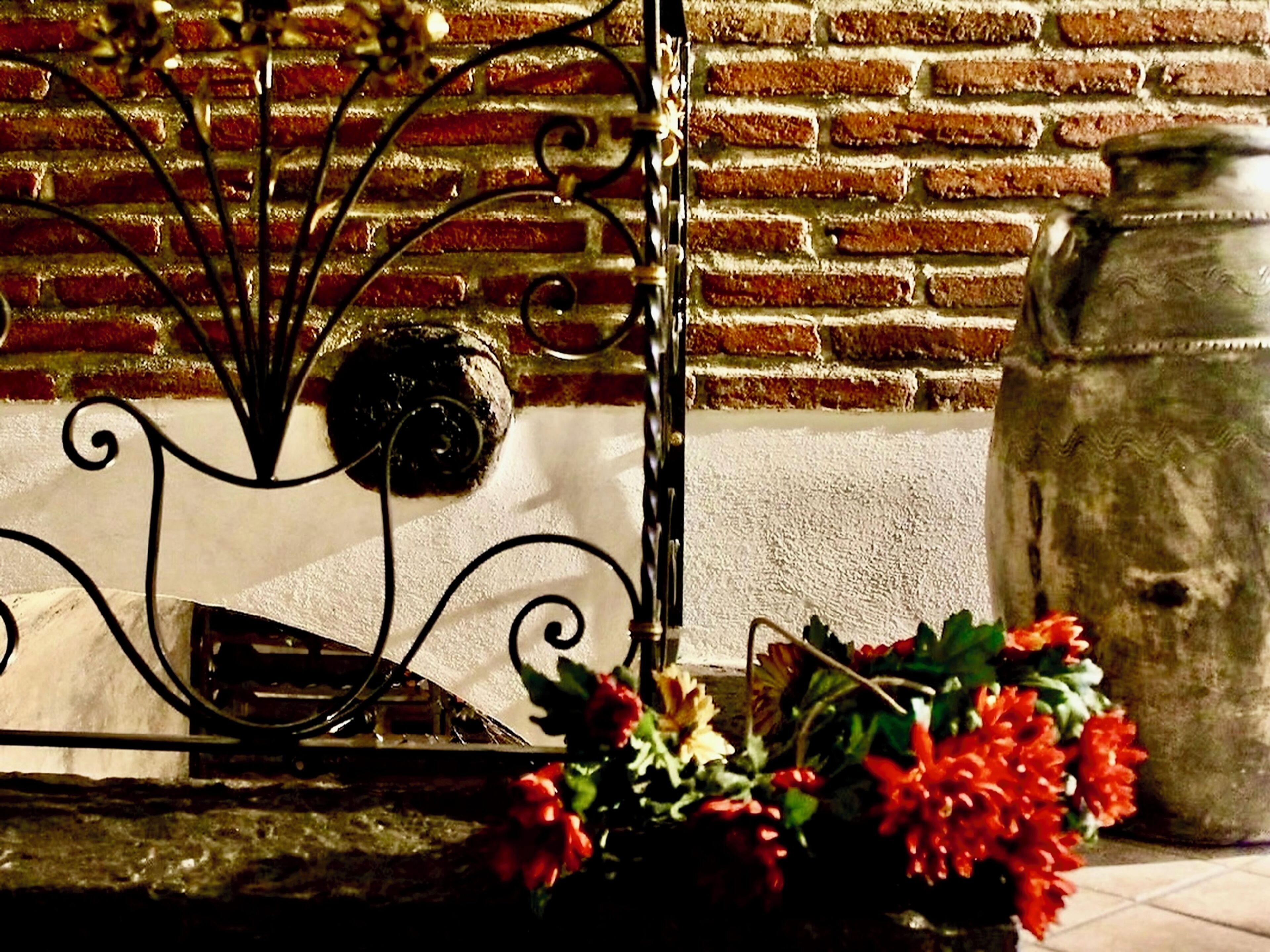 A brick wall with a metal railing and a vase of red flowers.