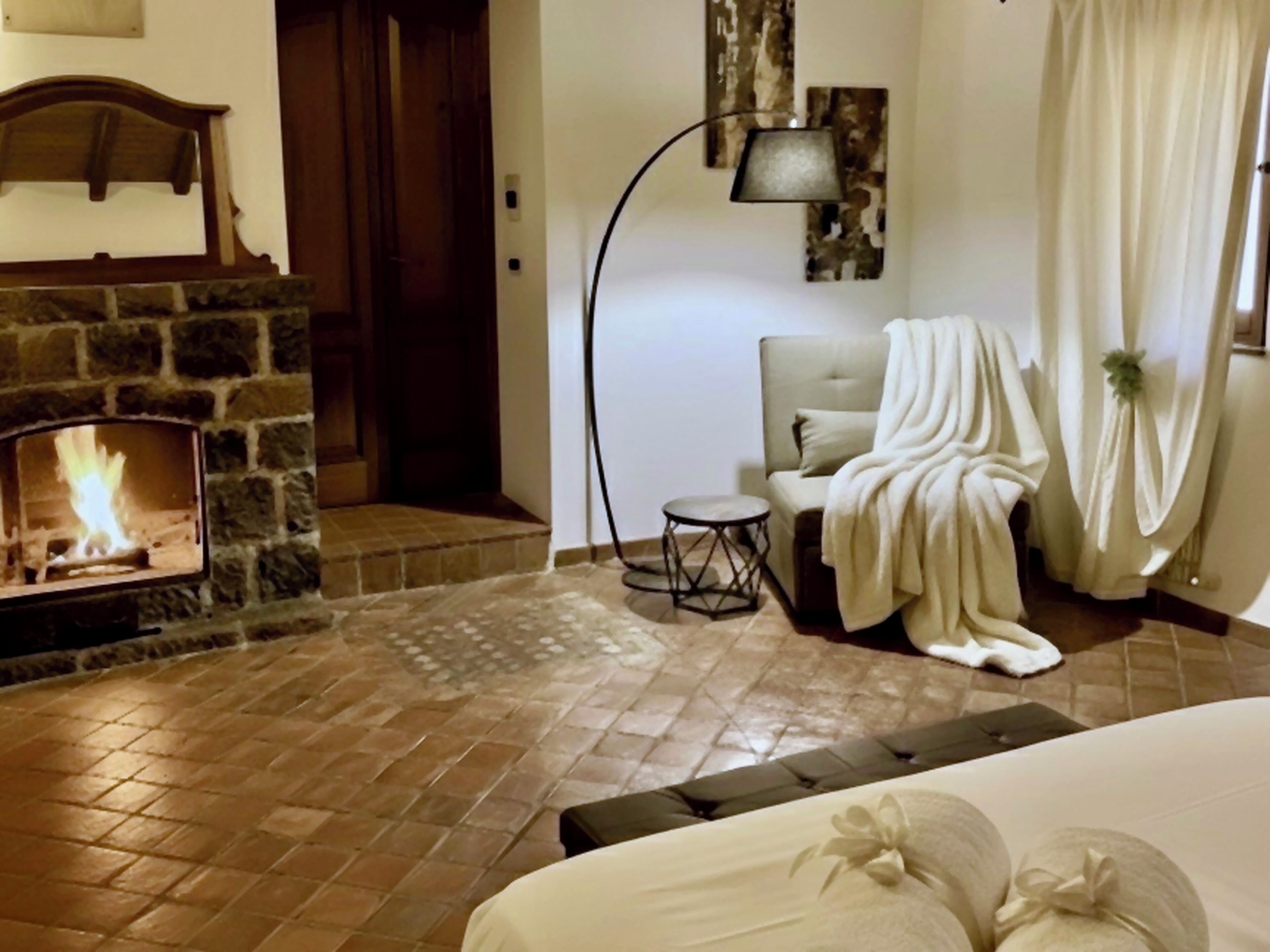 A cozy room with a stone fireplace, a comfortable chair, and a bed with floral pillows.