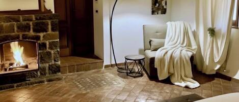 A cozy room with a stone fireplace, a comfortable chair, and a bed with floral pillows.