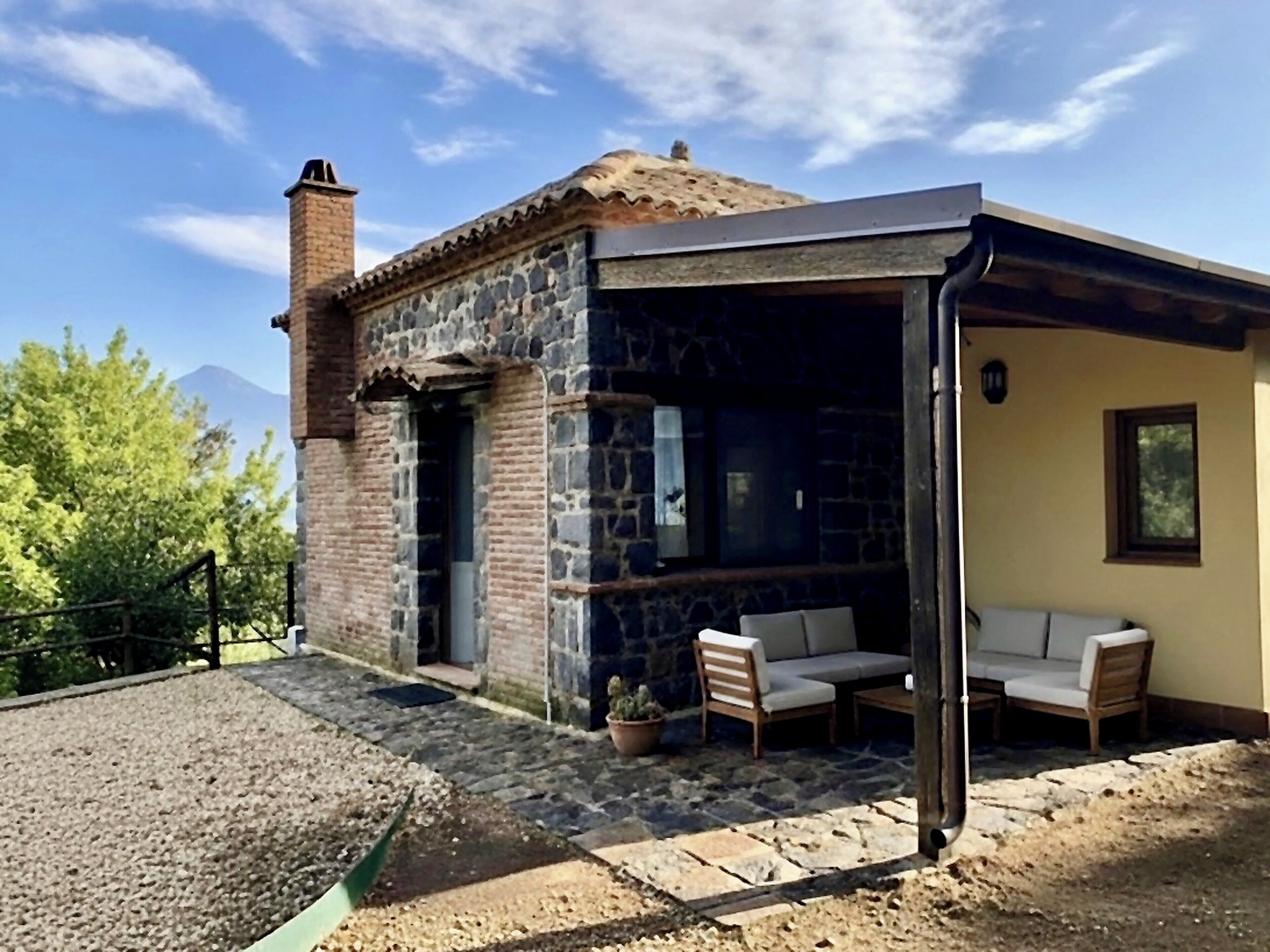 A stone building with a covered outdoor seating area, a chimney, and a view of a mountain.