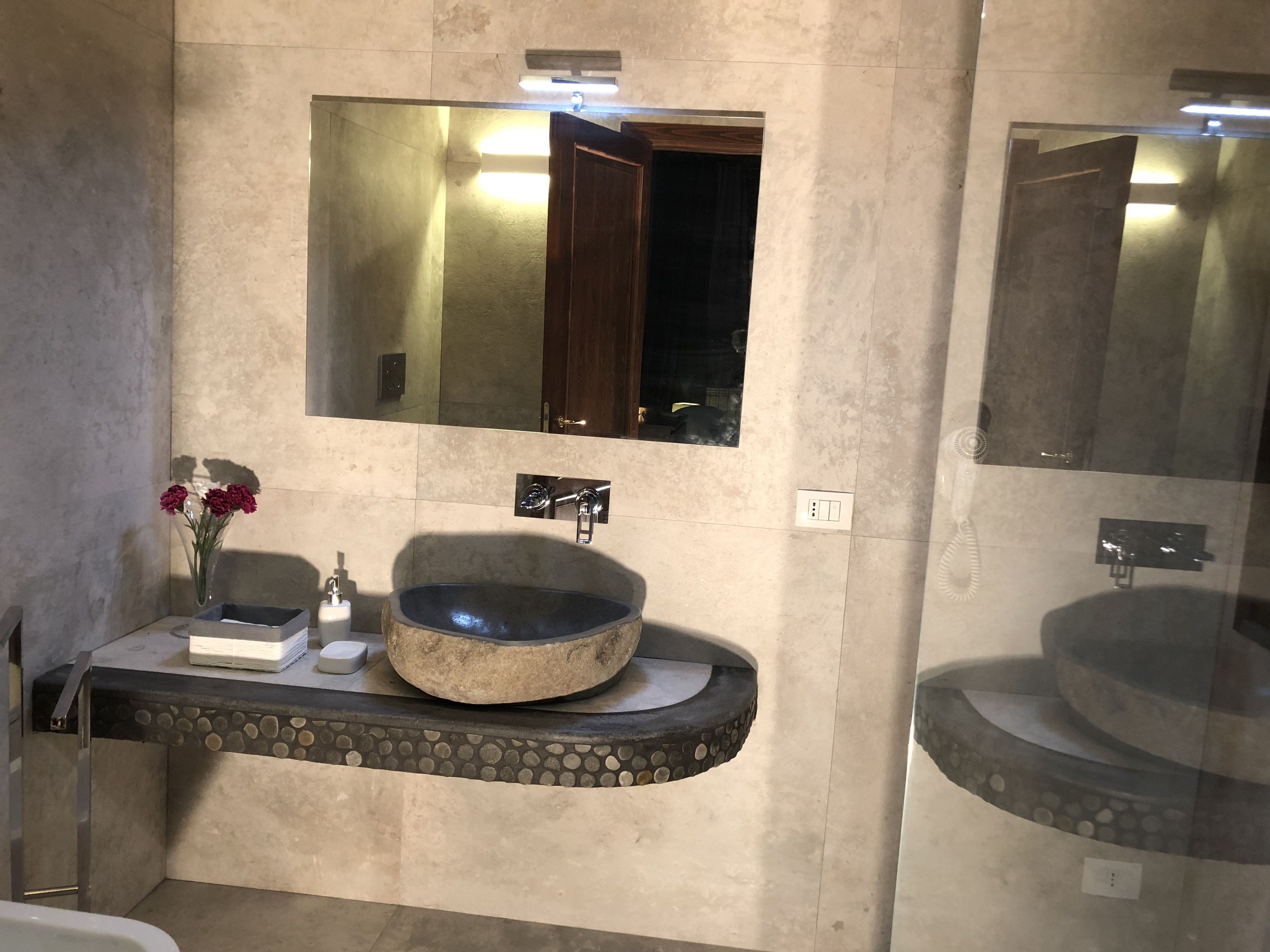 Un bagno con due lavandini, uno specchio e un vaso con fiori.