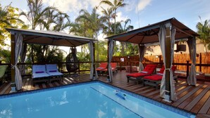 Un espace piscine doté de deux coins salon couverts, chacun comprenant des chaises longues et des parasols.