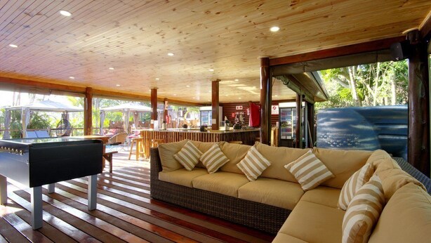 Une terrasse en bois avec un canapé et une table de billard, un coin bar et une vue sur la mer.