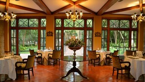 A dining area with tables set for four, large windows, and a central chandelier. - De Hoek Country Hotel (Magaliesberg)