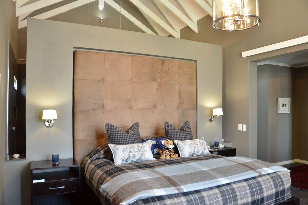 A bedroom with a large bed, two nightstands, a headboard, and wall-mounted lamps.