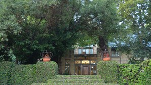 A stone building with a wooden door and windows, surrounded by lush greenery and a staircase leading up to it. - De Hoek Country Hotel (Magaliesberg)