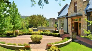 A stone building with a landscaped garden, a central circular driveway, and a well-maintained lawn. - De Hoek Country Hotel (Magaliesberg)