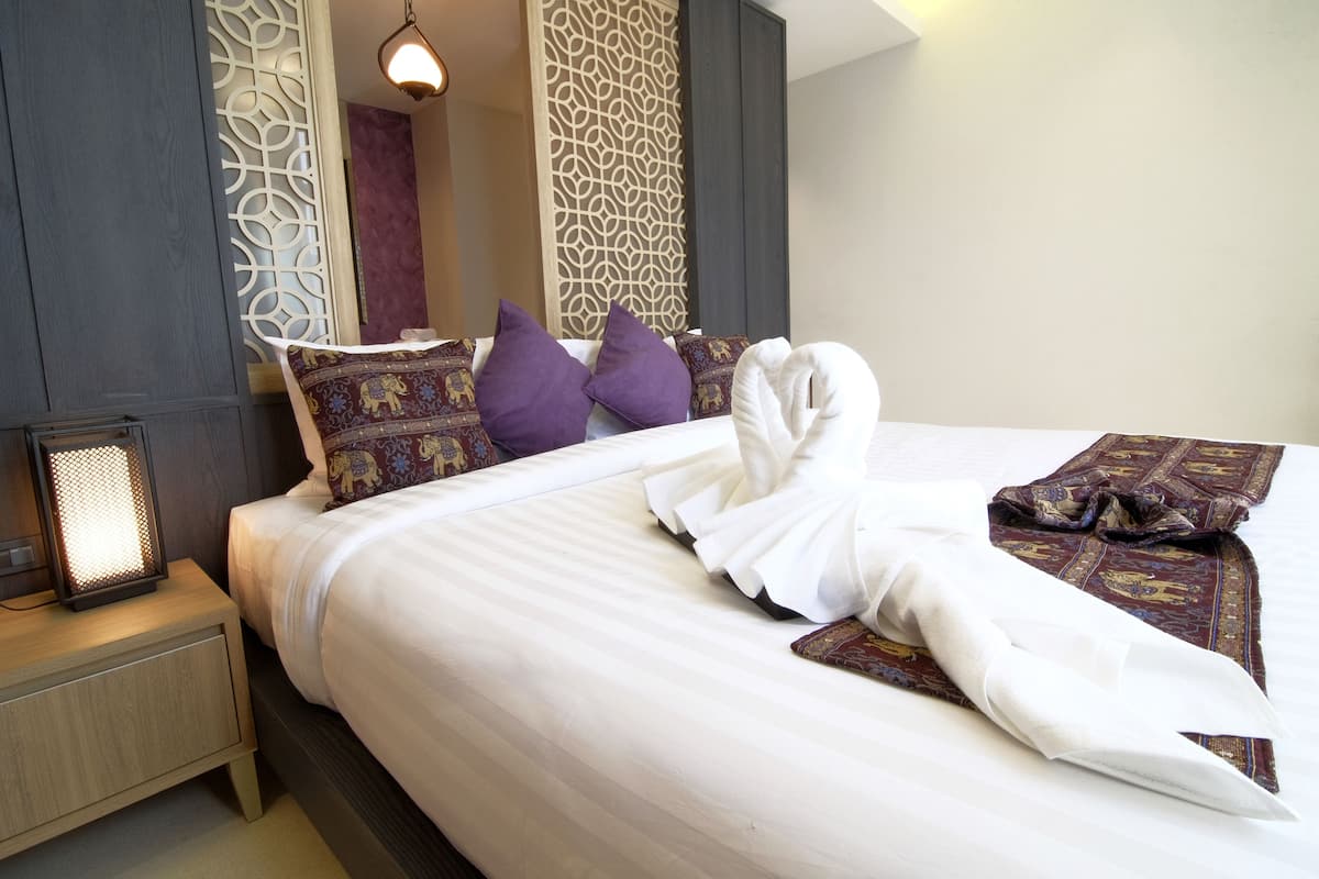 A neatly made bed with a white duvet, purple pillows, and a decorative blanket.