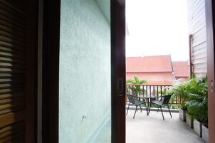 A balcony with a table and chairs, a potted plant, and a view of a red-roofed building in the background.