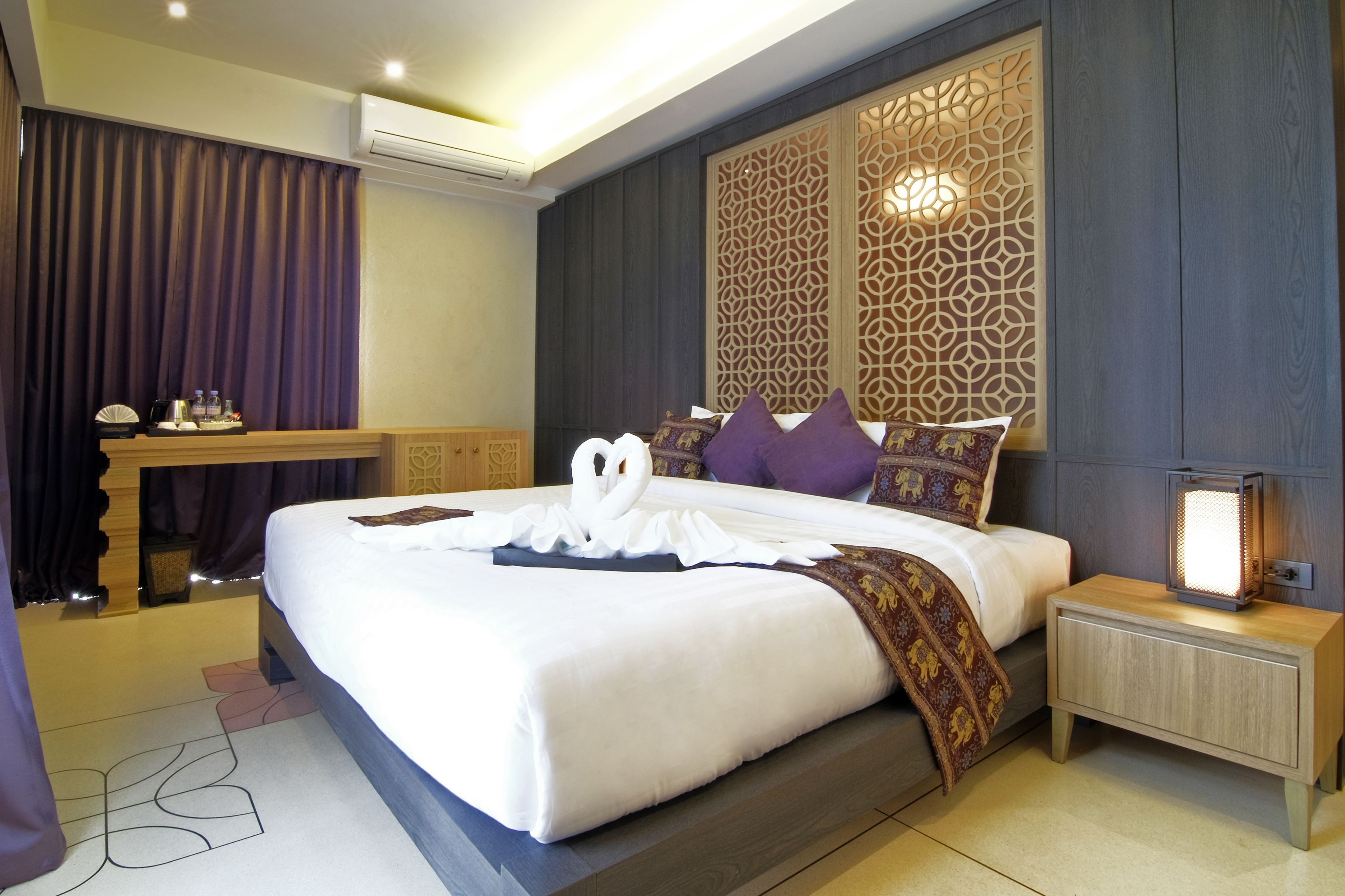 A modern hotel room with a large bed, a bedside table, a nightstand, and a decorative wall panel.