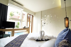 A hotel room with a bed, a TV, a window with a view of palm trees, and a decorative wall.