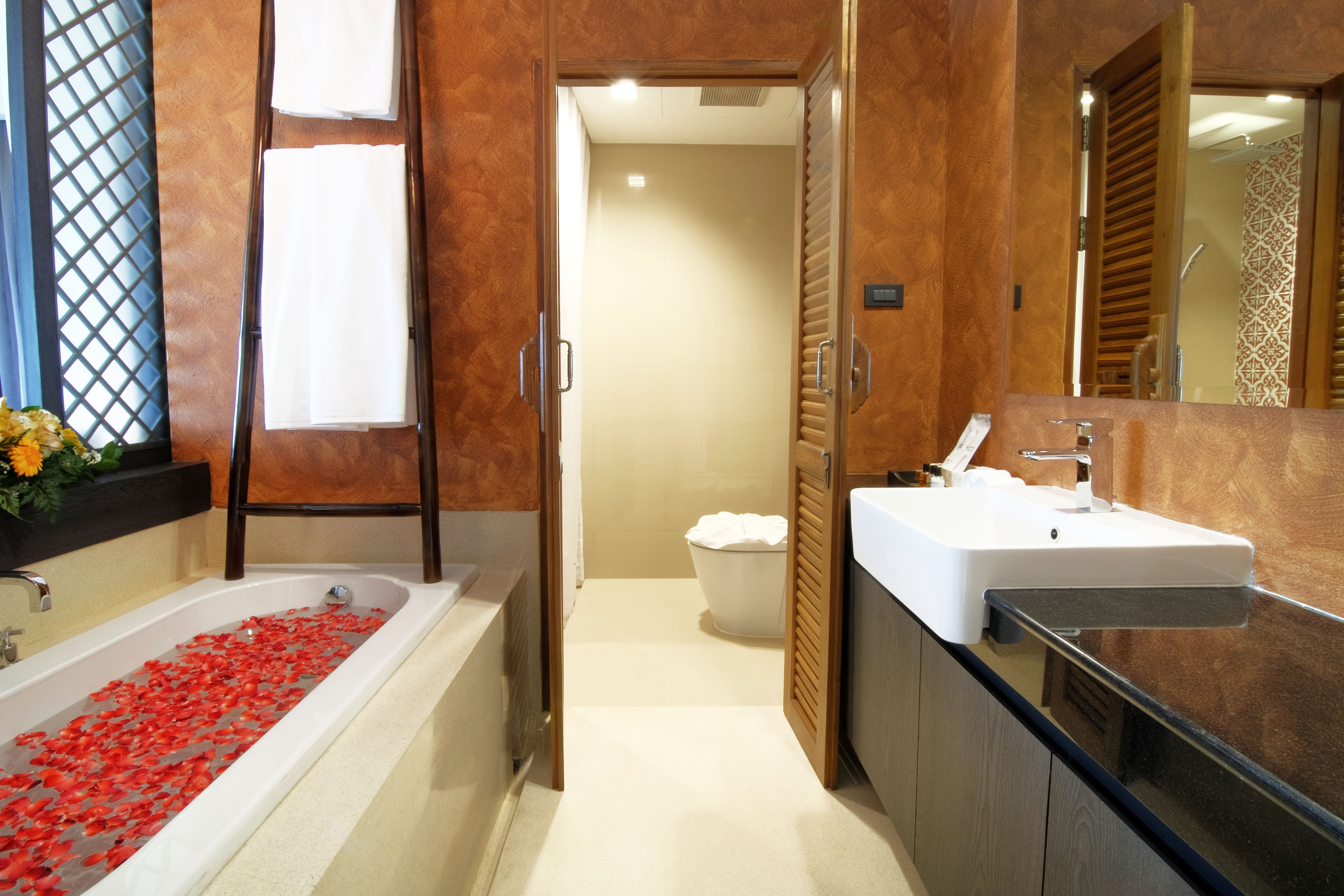 Un baño moderno con una bañera llena de pétalos de rosa, un espejo grande y un lavamanos.
