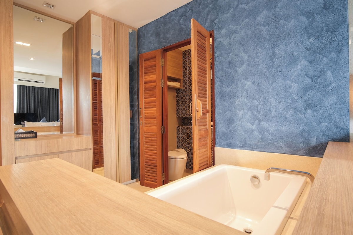 A modern bathroom with a wooden vanity, a bathtub, and a walk-in closet with sliding doors.
