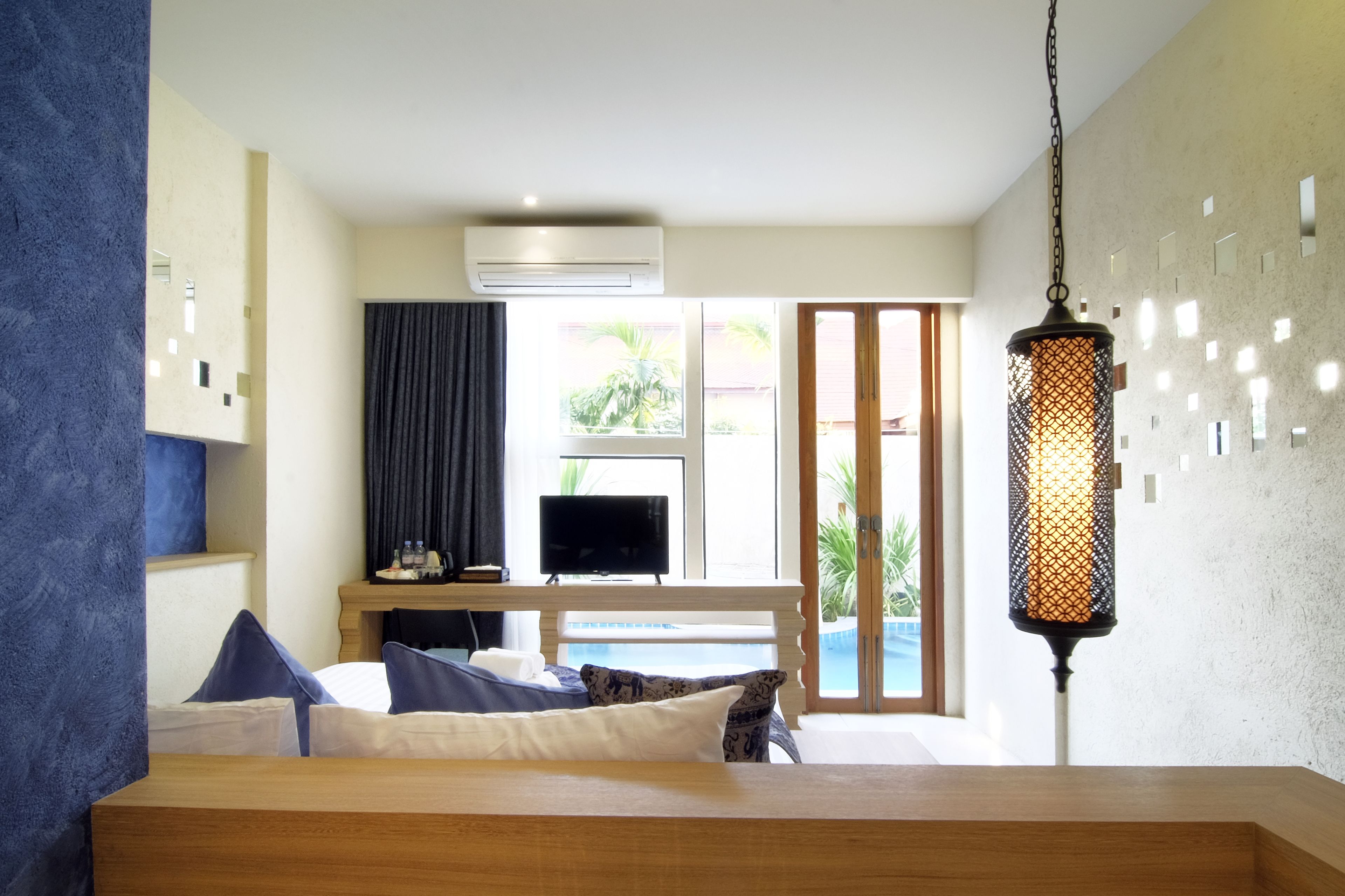 A hotel room with a bed, a TV, a desk with a computer, a hanging lamp, and a view of the outdoors.