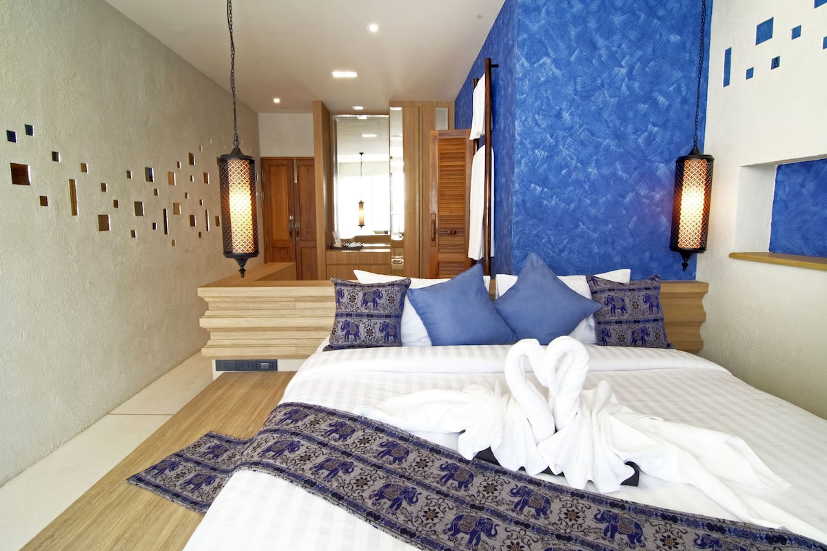 A hotel room with a large bed, wooden headboard, blue patterned pillows, and a blue textured wall.