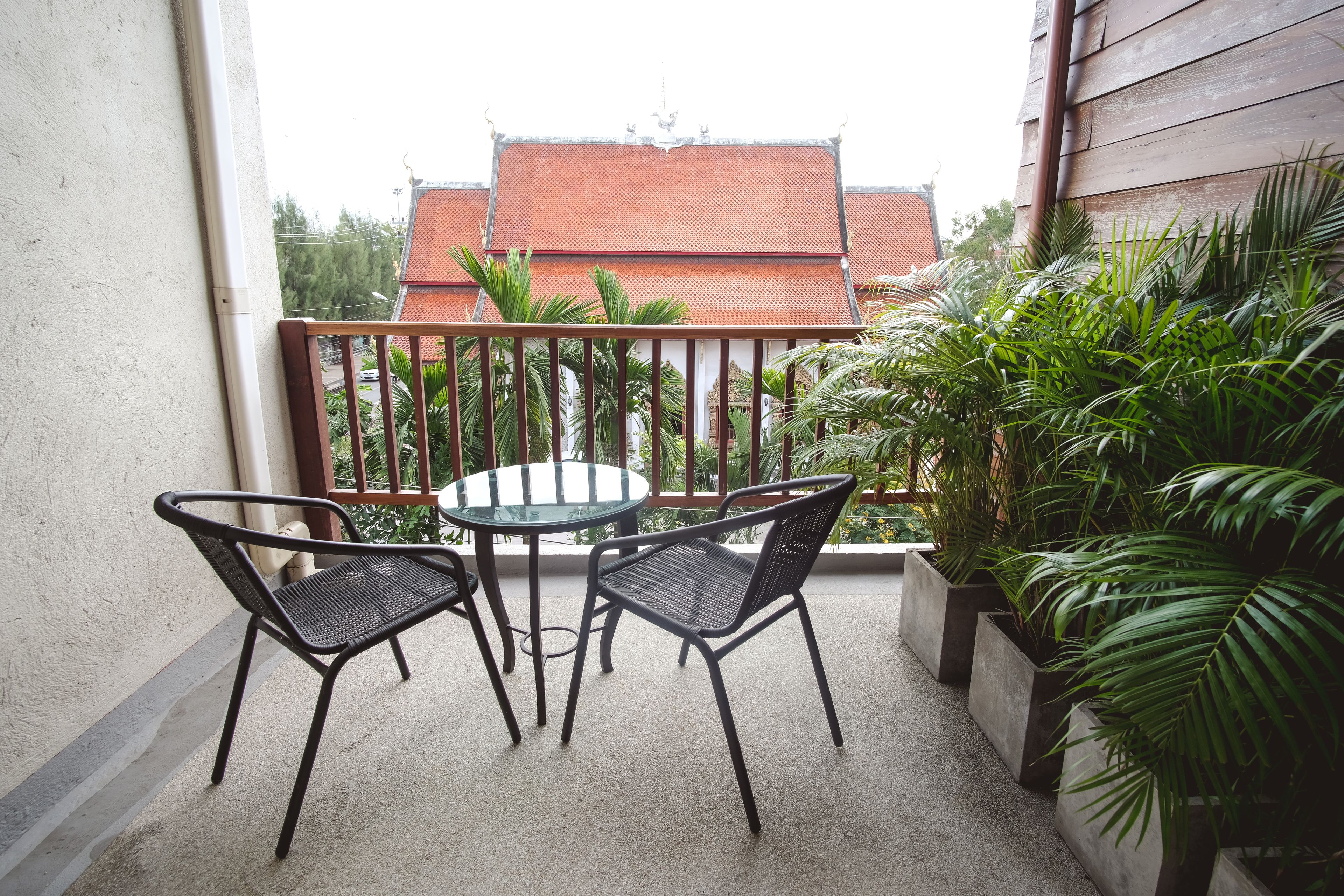 En balkon med et rundt bord og to stole, omgivet af krukker med planter.