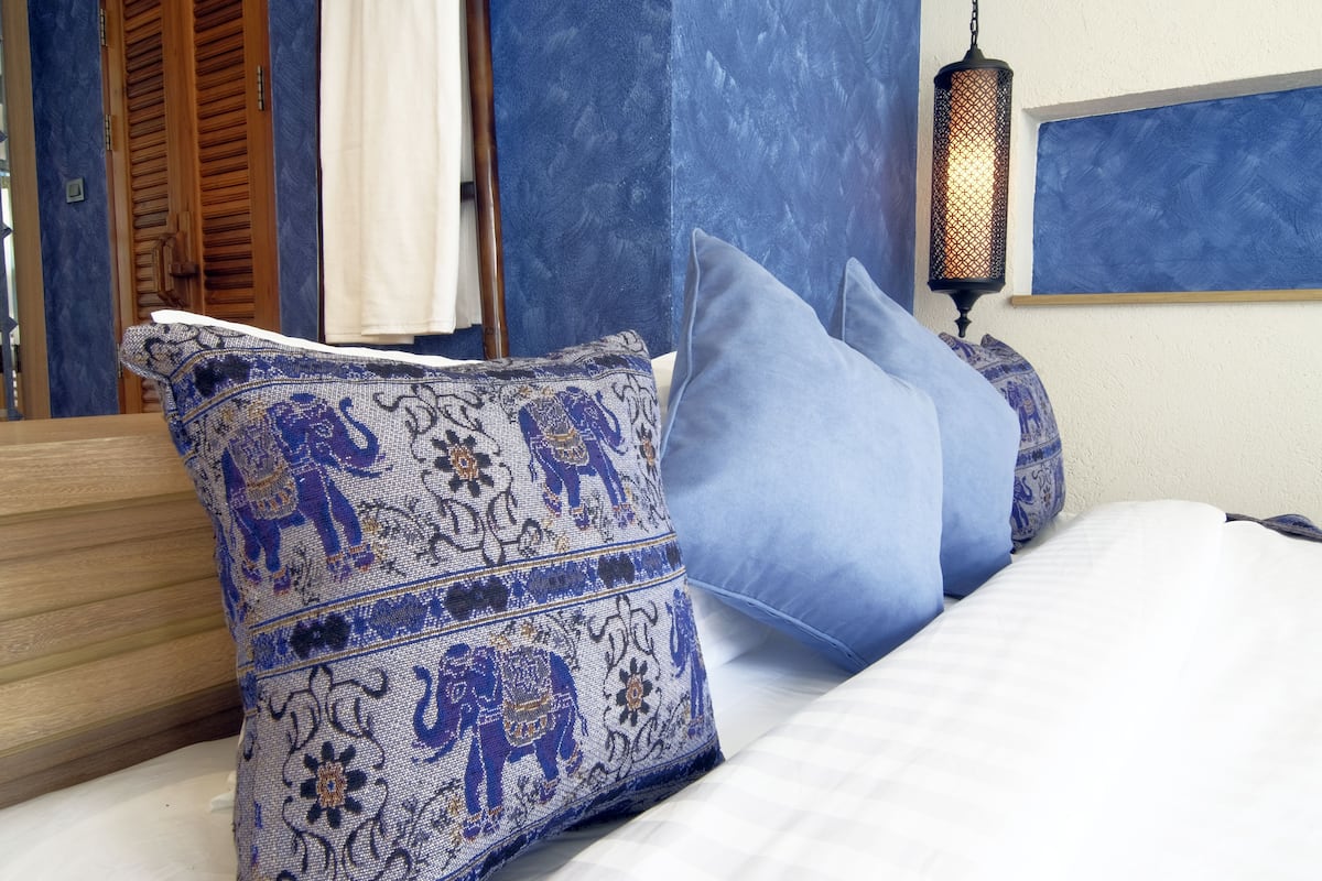 A bed with blue and patterned pillows, a hanging lantern, and a wooden headboard.