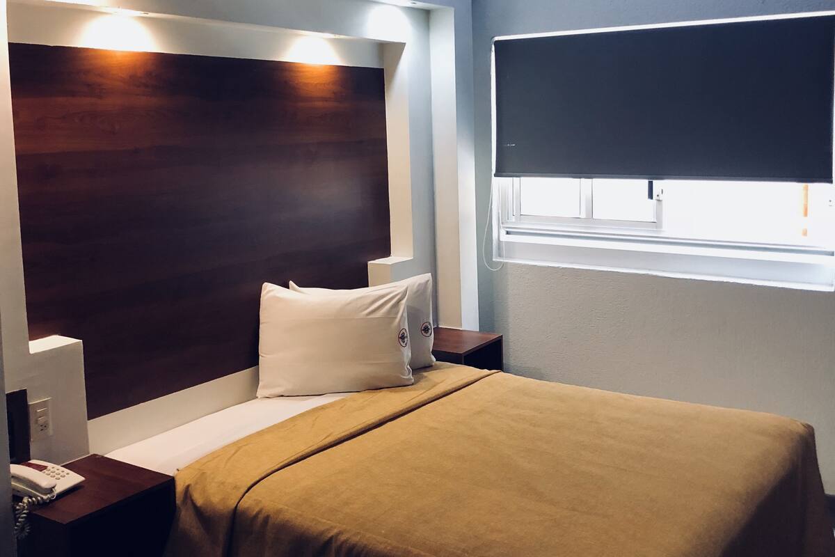 A hotel room with a bed, bedside table, and a window.