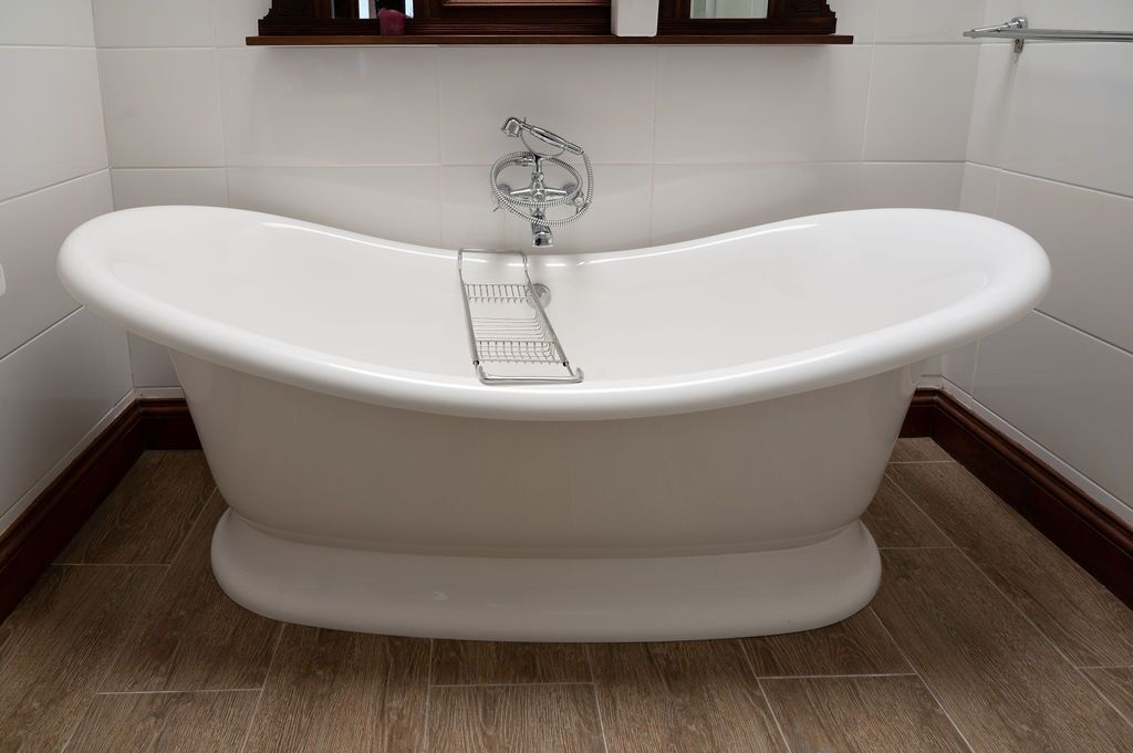 A freestanding bathtub in a bathroom with white tiles and wooden flooring.