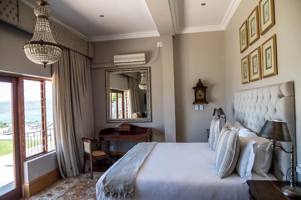 A bedroom with a large bed, a desk, a mirror, and a view of the outdoors.