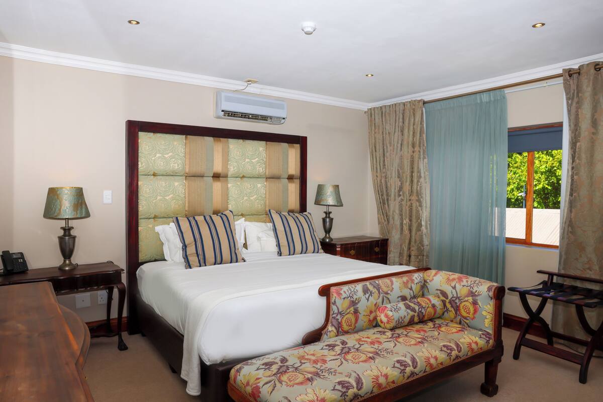 A hotel room with a large bed, a sofa, a desk, and a window with curtains.
