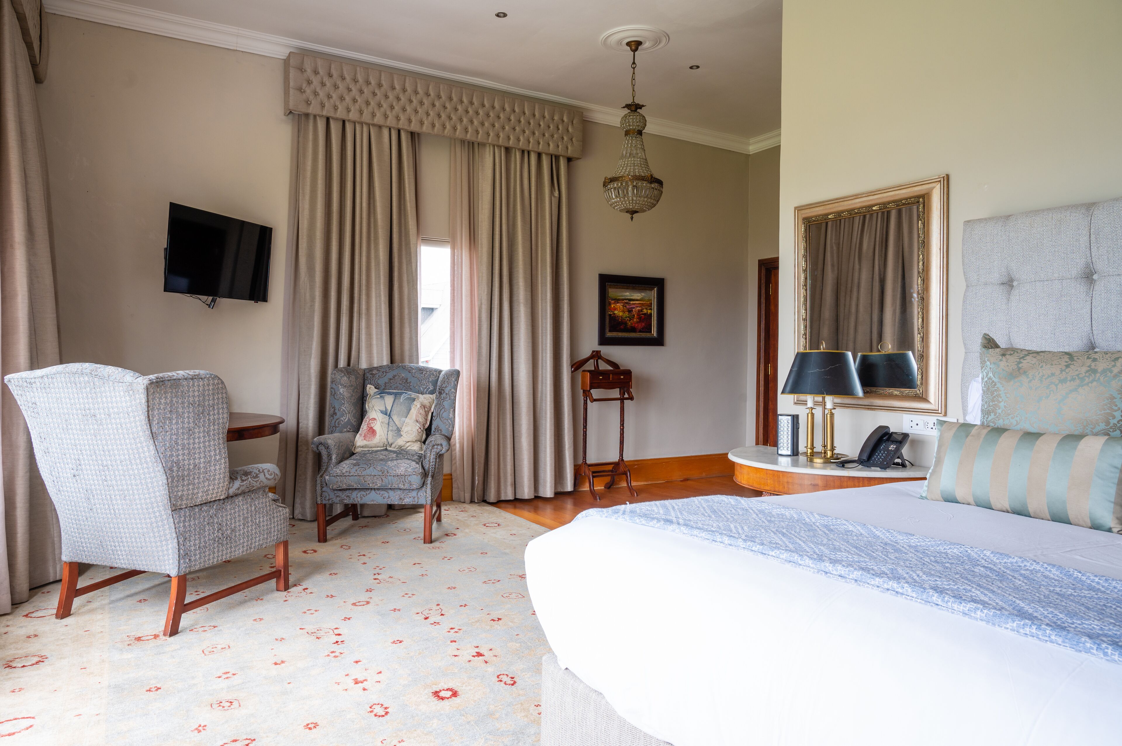 A hotel room with a large bed, a chair, a desk, a television, and a chandelier.