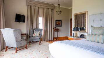 A hotel room with a large bed, a chair, a desk, a television, and a chandelier.