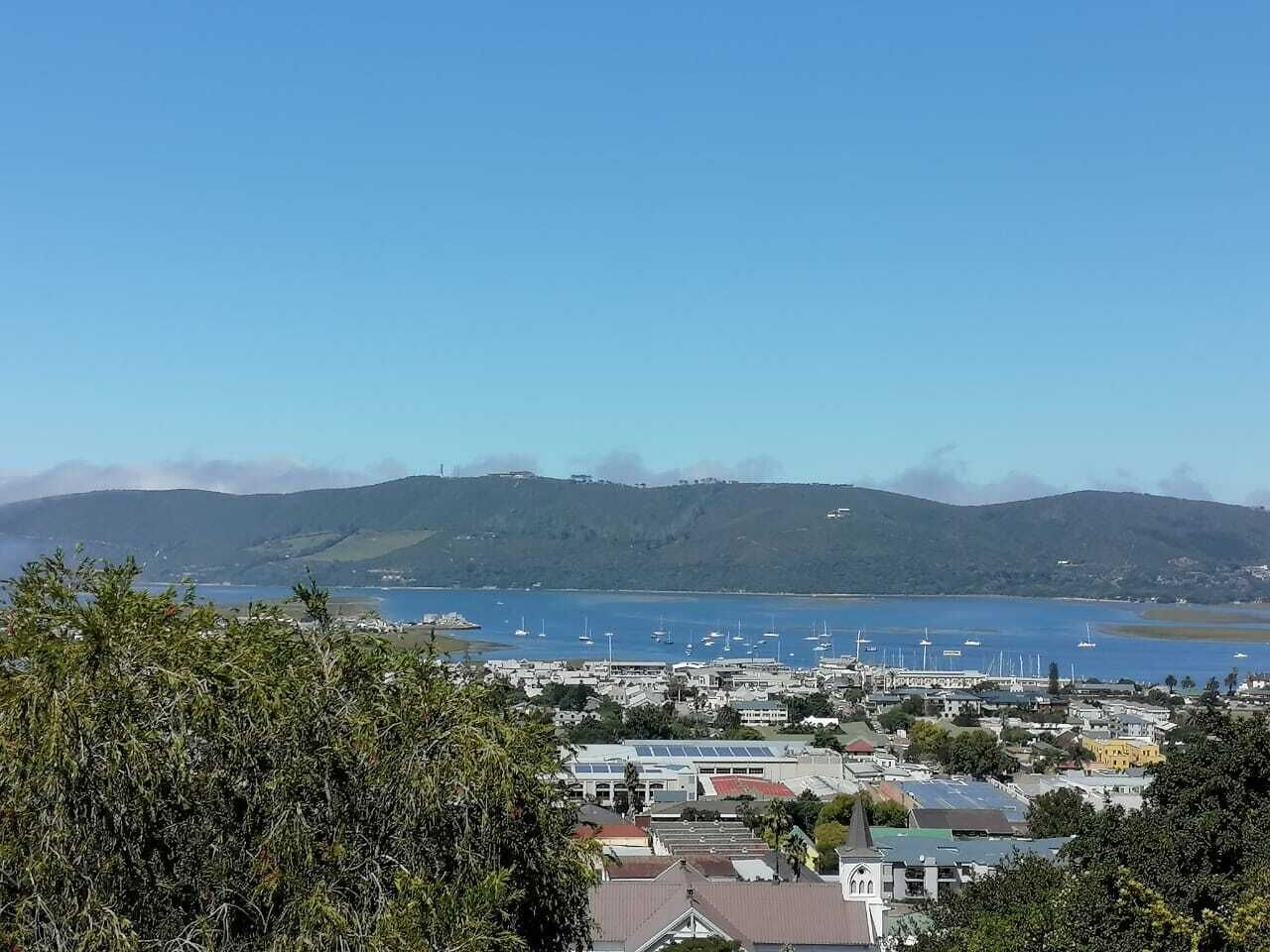 A coastal town with a marina, buildings, and hills in the background.