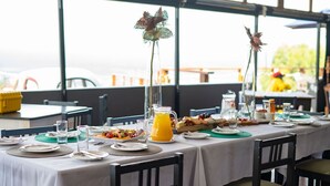 Mesa de café da manhã posta com pratos, copos e um jarro de suco de laranja, com vista para o exterior.
