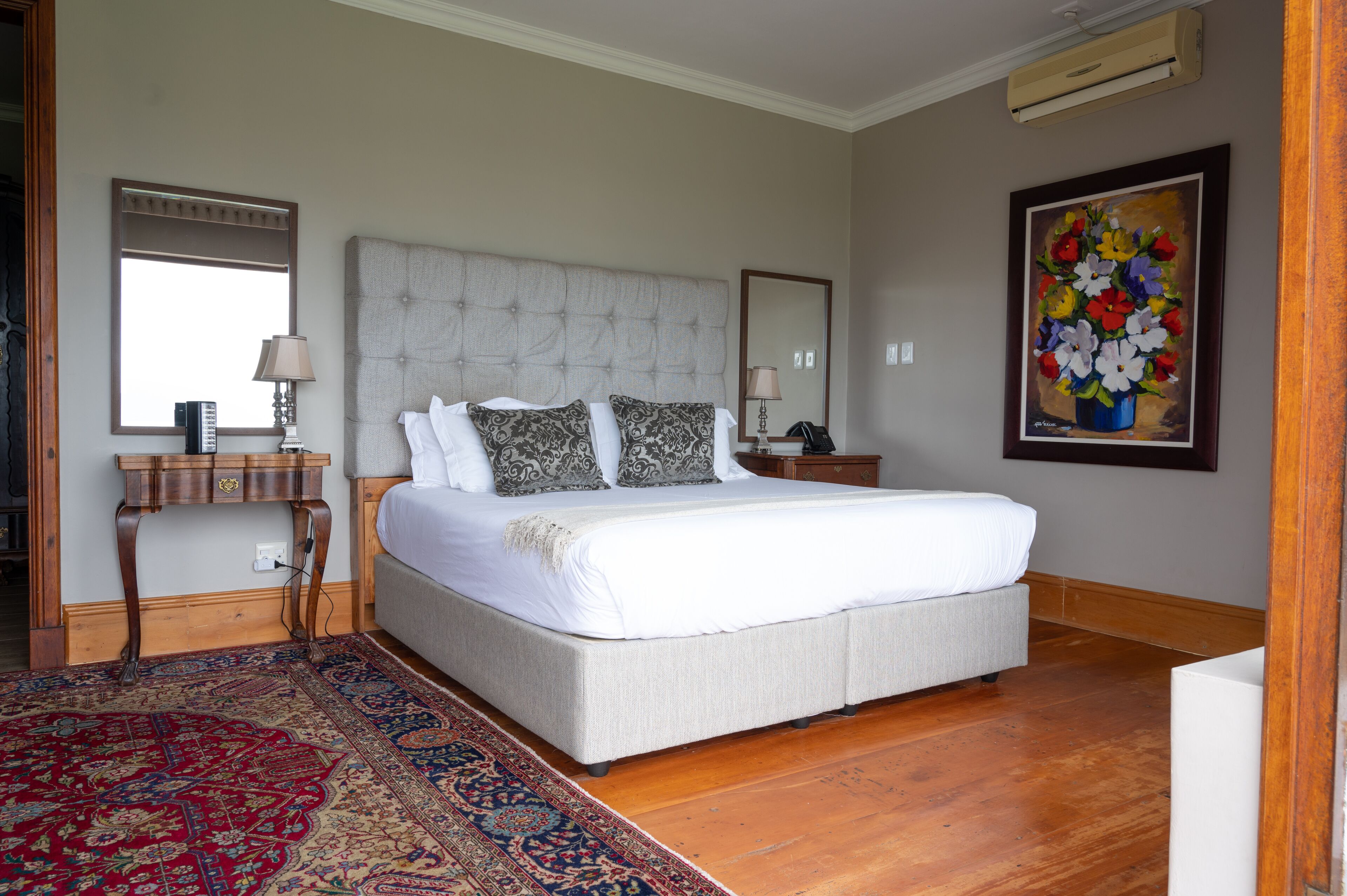 Une chambre à coucher avec un grand lit, une table de chevet, une commode, un miroir, un tableau et un tapis à motifs.