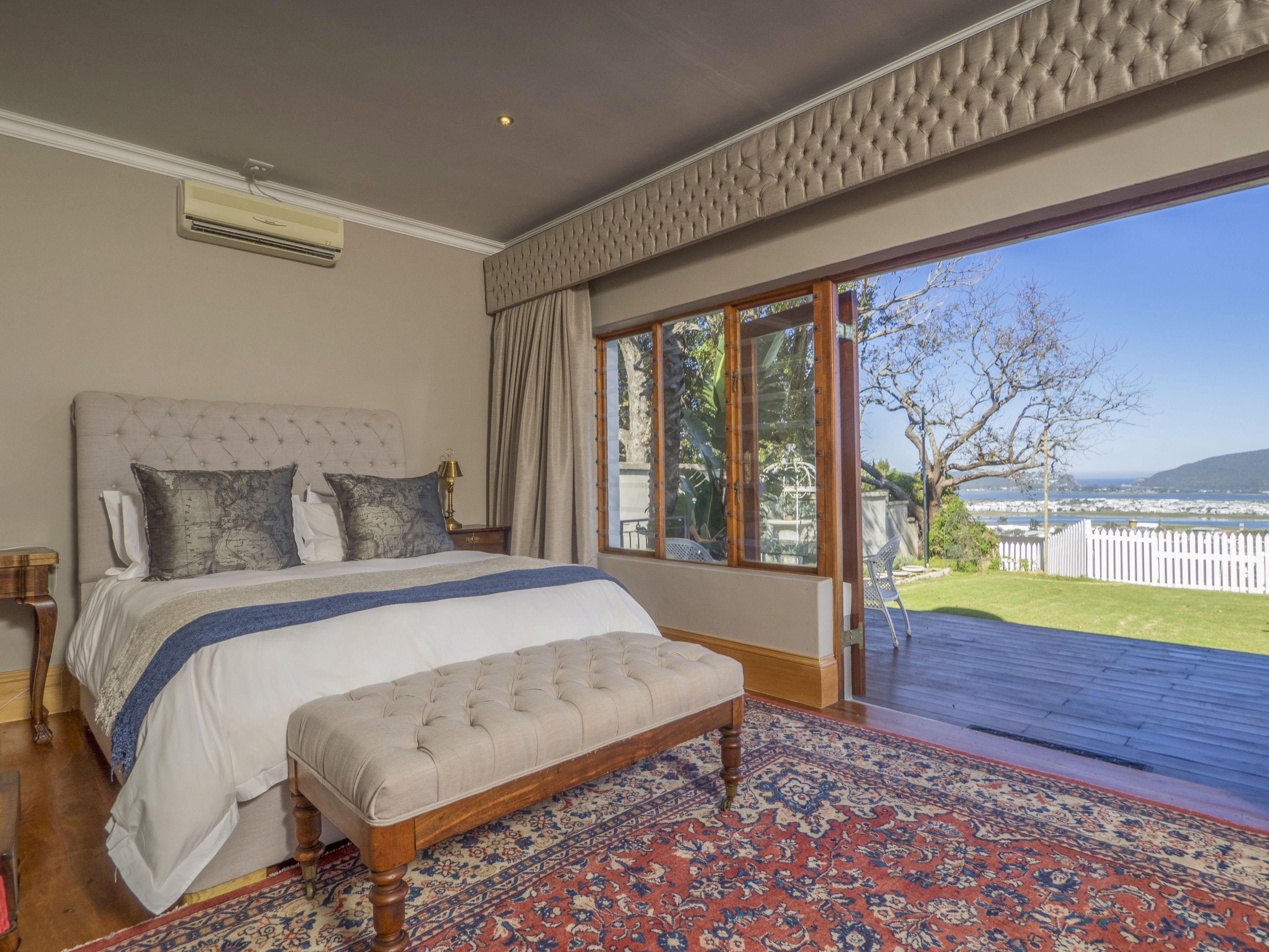 A bedroom with a large bed, a bench, and a view of the outdoors.
