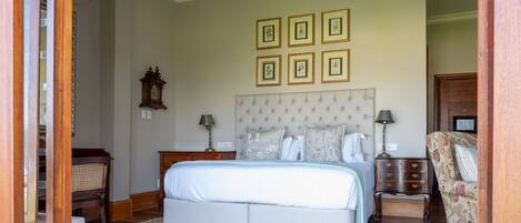 Un dormitorio con una cama grande, una mesita de noche, un aparador, una silla y una lámpara de araña.
