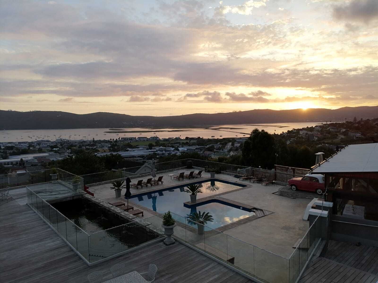 Zona de piscina en la azotea con vista a una masa de agua y colinas distantes al atardecer.