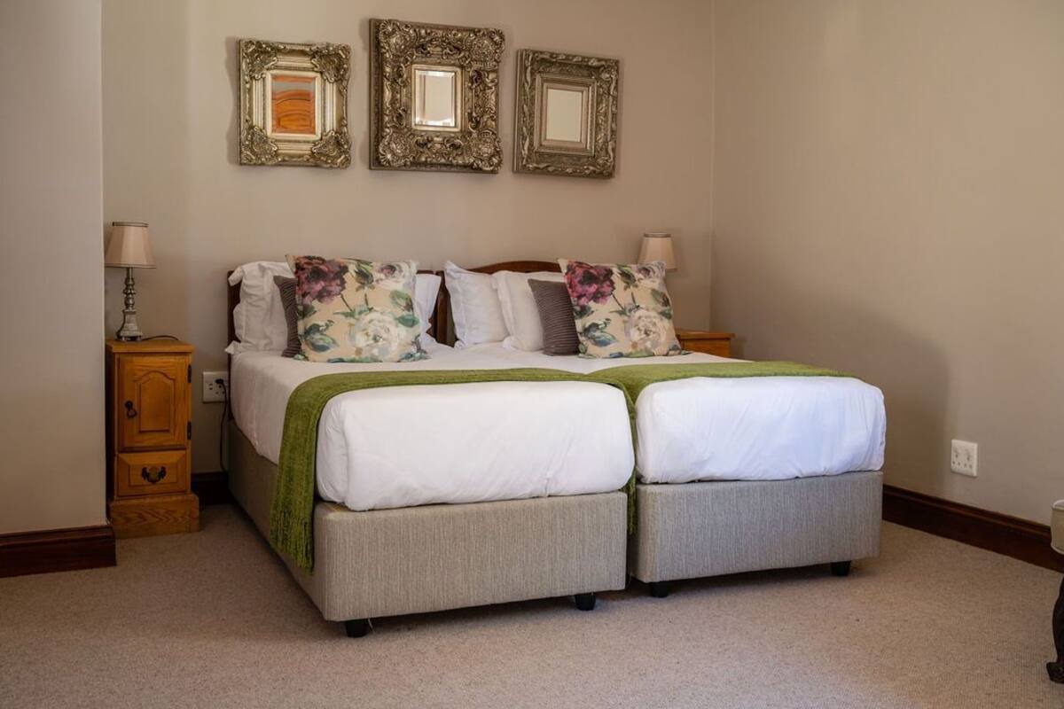 A double bed with a green throw blanket, two bedside tables with lamps, and three framed mirrors on the wall.