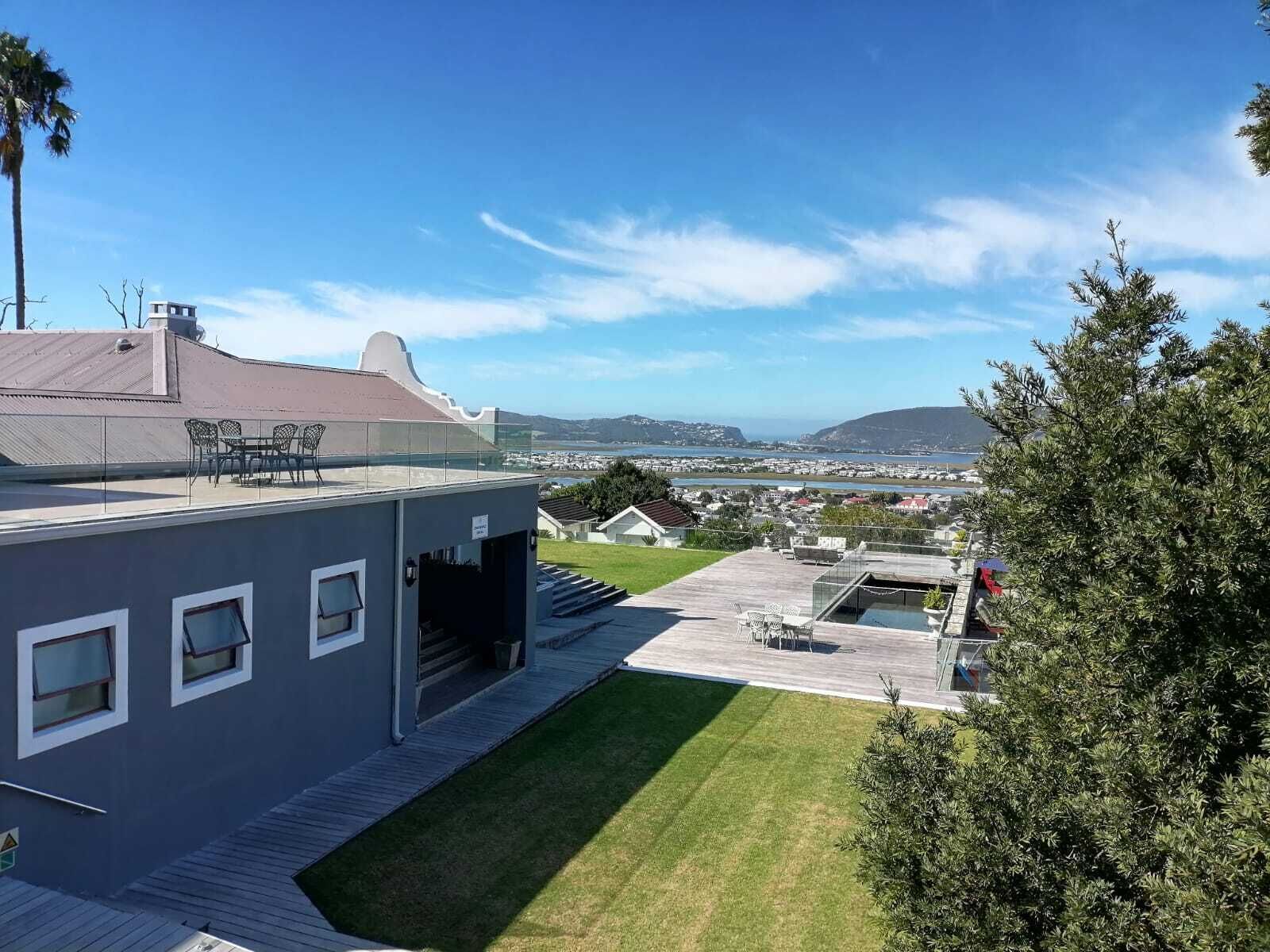 A modern building with a flat roof, a covered patio with outdoor seating, and a view of a coastal landscape.