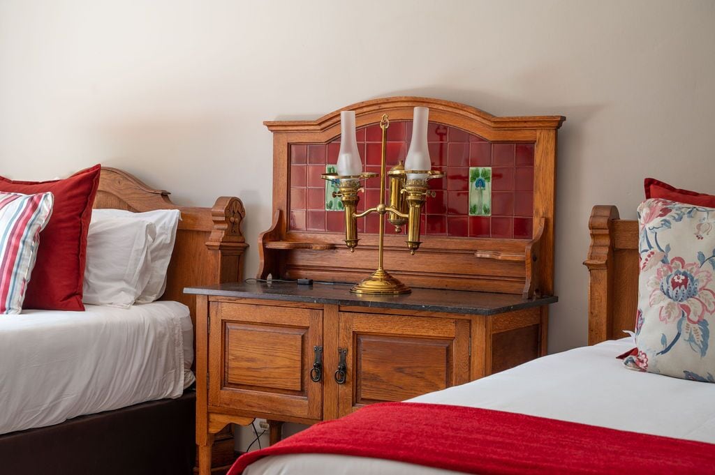 Quarto de hotel com duas camas, um aparador de madeira e uma luminária fixada na parede.