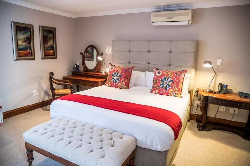 Un dormitorio con una cama grande, una mesita de noche de madera, un escritorio y dos cuadros en la pared.