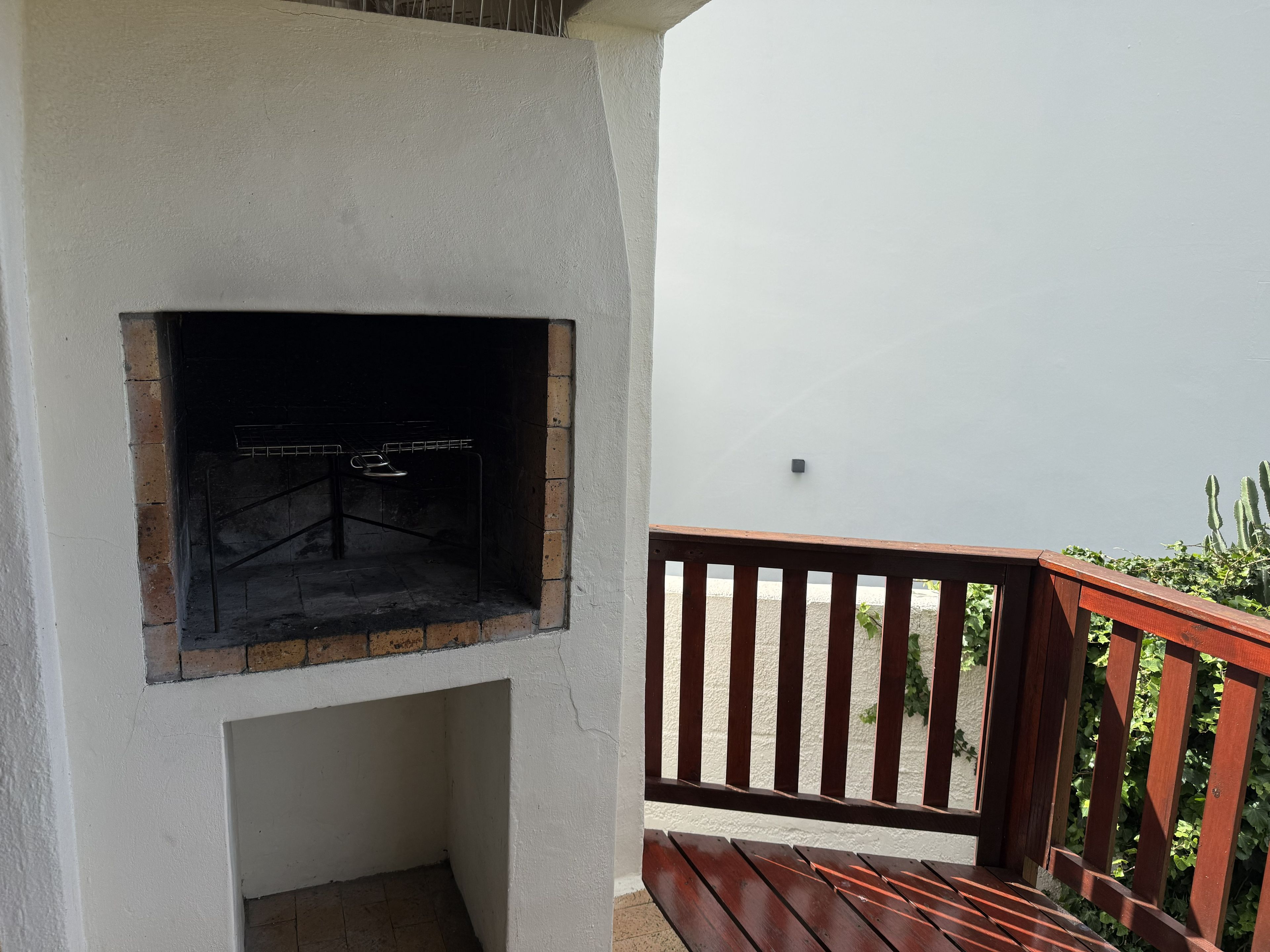 Un espace barbecue extérieur en briques, avec un banc en bois et une rambarde.
