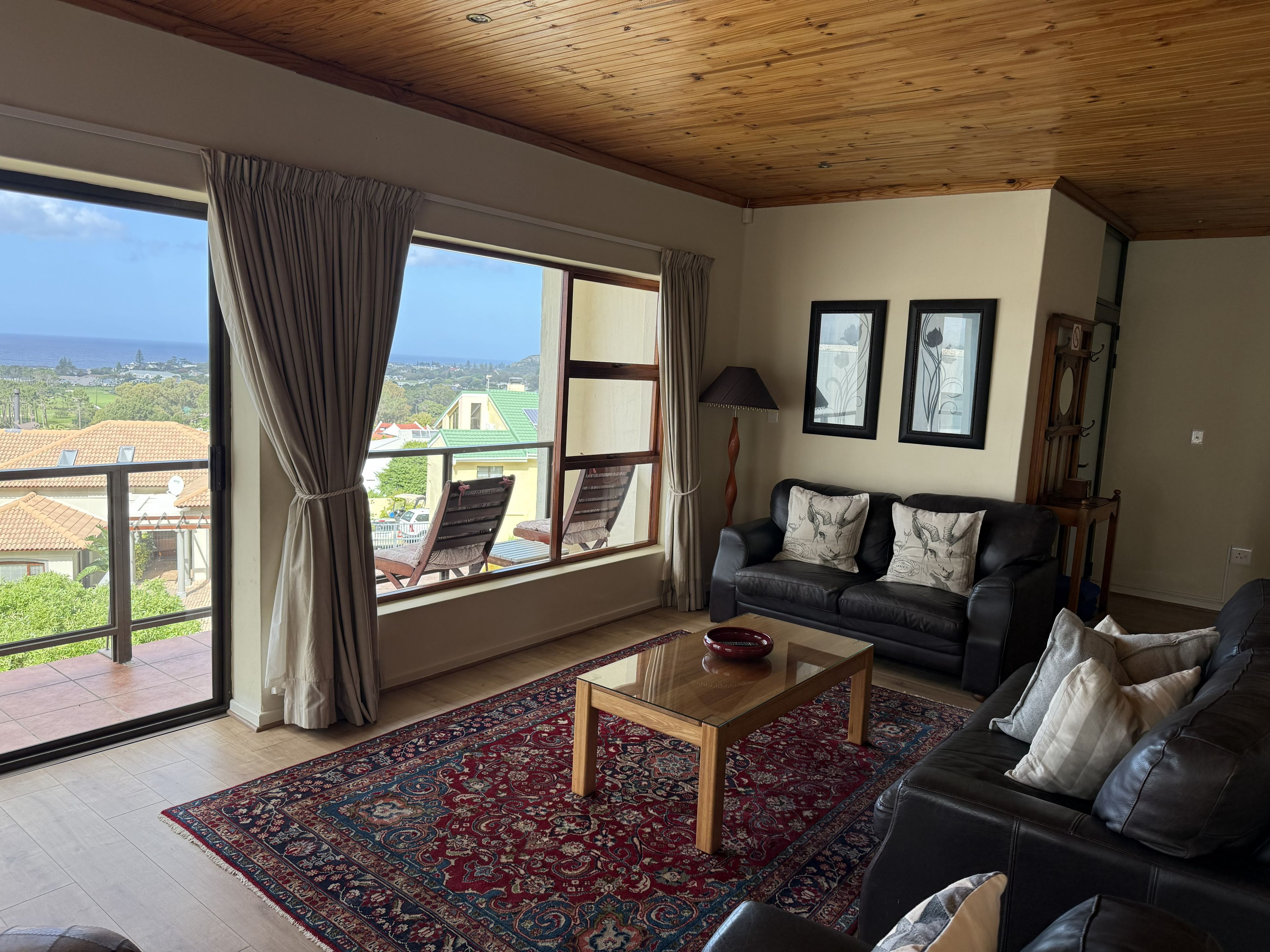 Sala de estar com uma grande janela, sofá de couro preto, mesa de centro de madeira e tapete estampado.