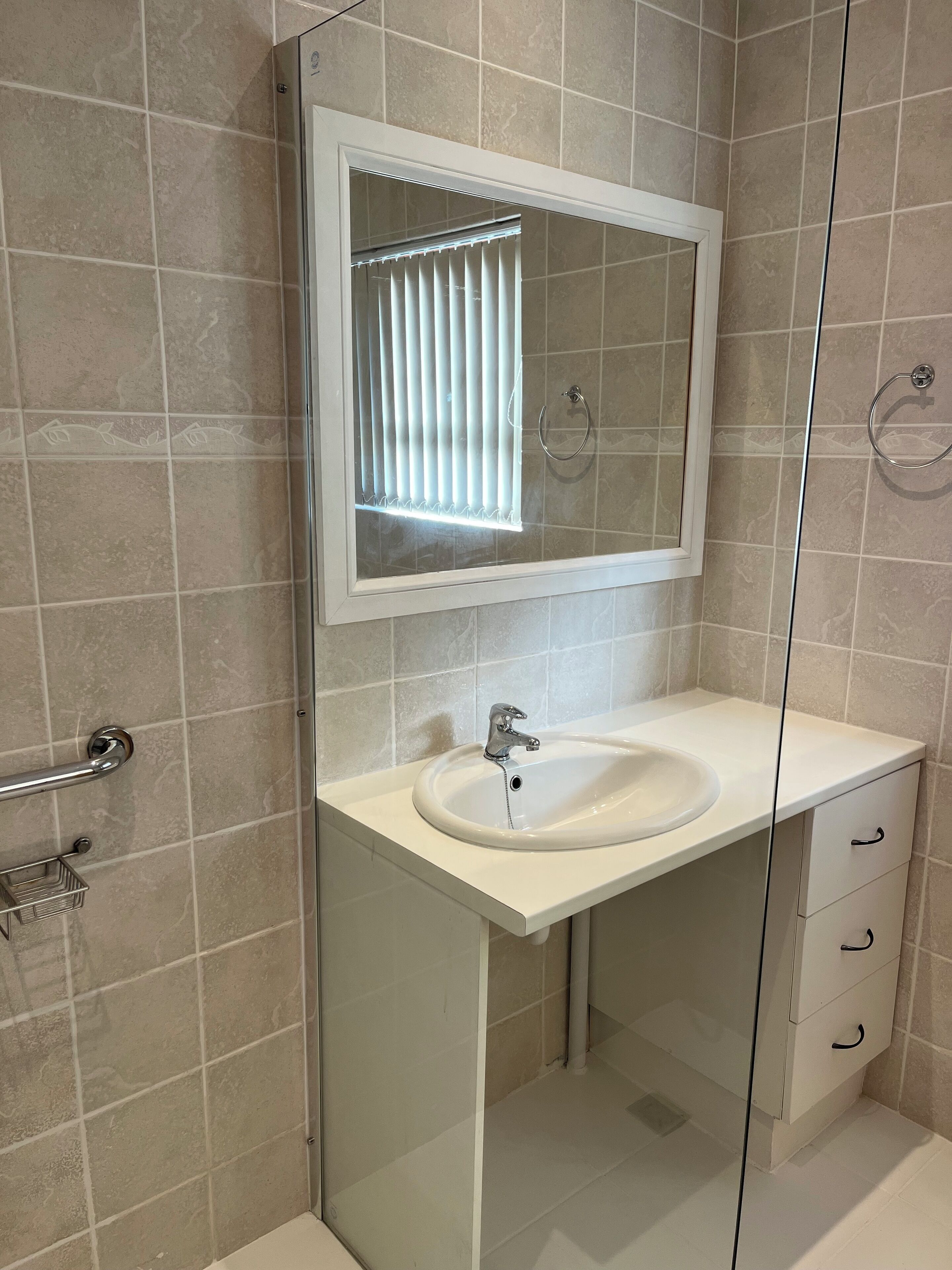 Ein Badezimmer mit einem weißen Waschbecken, einem Spiegel und einer Duschkabine aus Glas.