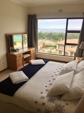 A hotel room with a large bed, a desk, a chair, a mirror, and a view of the surrounding area. - Hermanus Heights Villa (Hermanus)