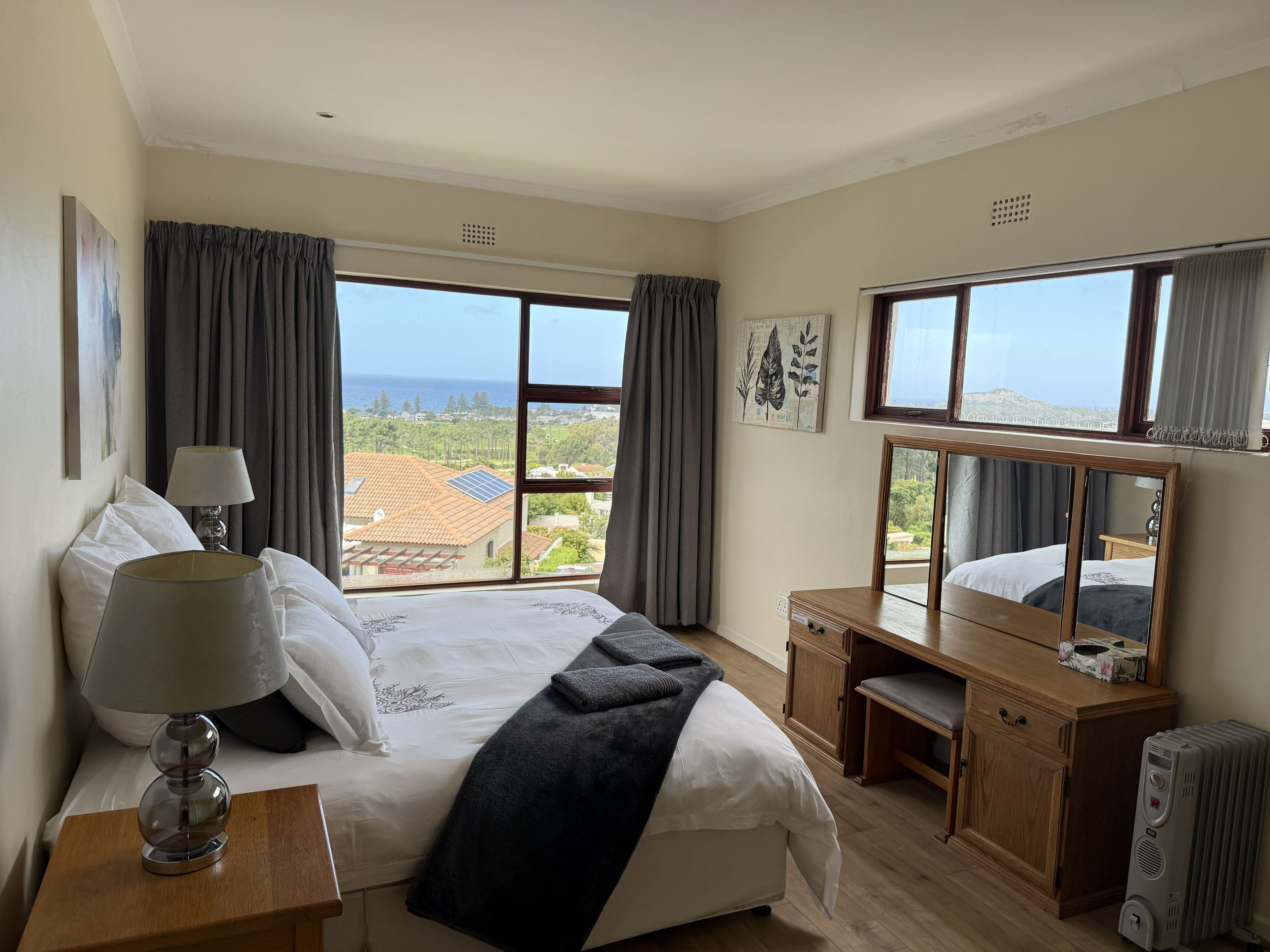 Habitación de hotel con cama, mesitas de noche, un escritorio, un espejo y vista al mar.