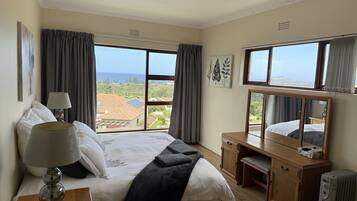 Habitación de hotel con cama, mesitas de noche, un escritorio, un espejo y vista al mar.