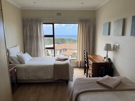 Habitación de hotel con cama, escritorio, silla, lámpara y vista al mar.