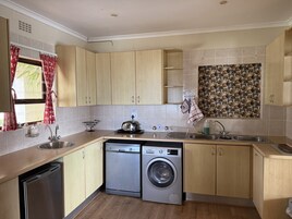 Cocina compacta con muebles de madera, lavadora Bosch, un lavamanos y una ventana con cortinas rojas.