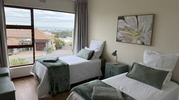 Une chambre d’hôtel avec deux lits, une table de chevet, une fenêtre donnant sur des immeubles et un tableau au mur.