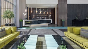 Um lobby moderno com balcão de recepção, área de estar e plantas decorativas.