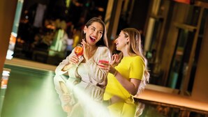Duas pessoas segurando bebidas em um bar com piscina ao fundo.